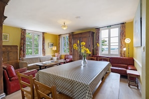 A dining area with a table, chairs, a vase with flowers, and a sofa.