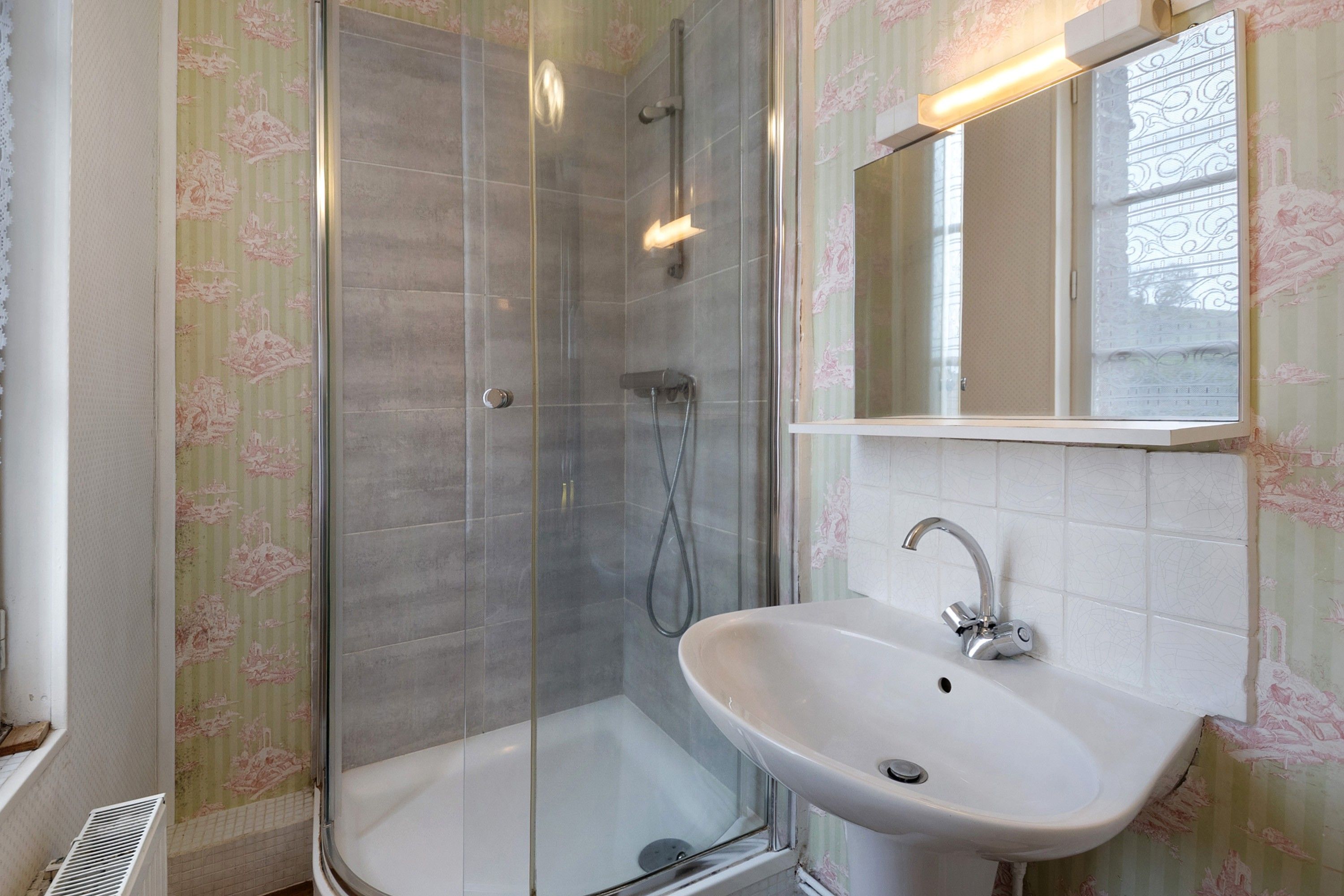 A bathroom with a glass-enclosed shower, a white sink, and a mirror above it.
