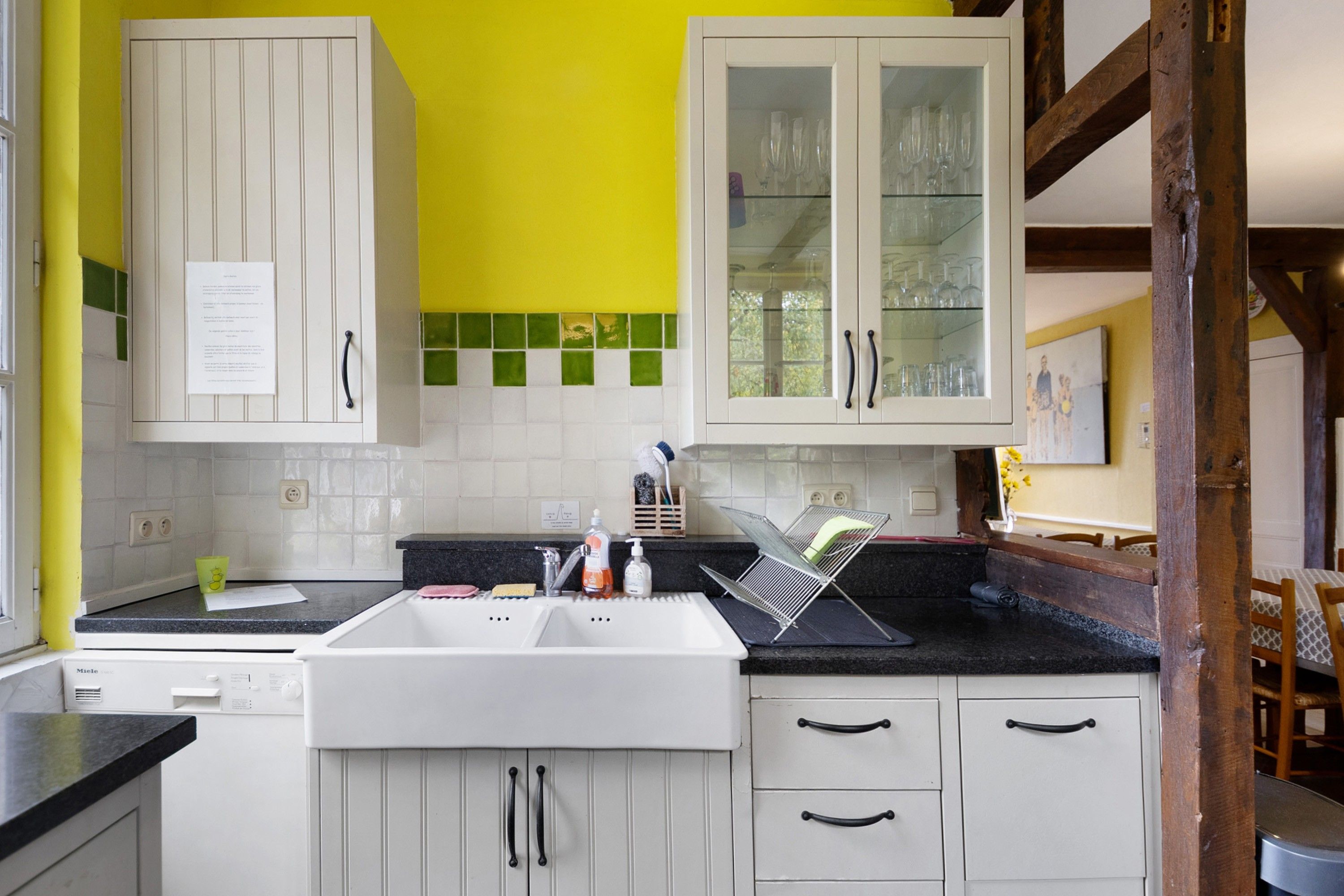 Una cocina con armarios blancos, un lavamanos y una encimera. Se ve una ventana con vistas a árboles.