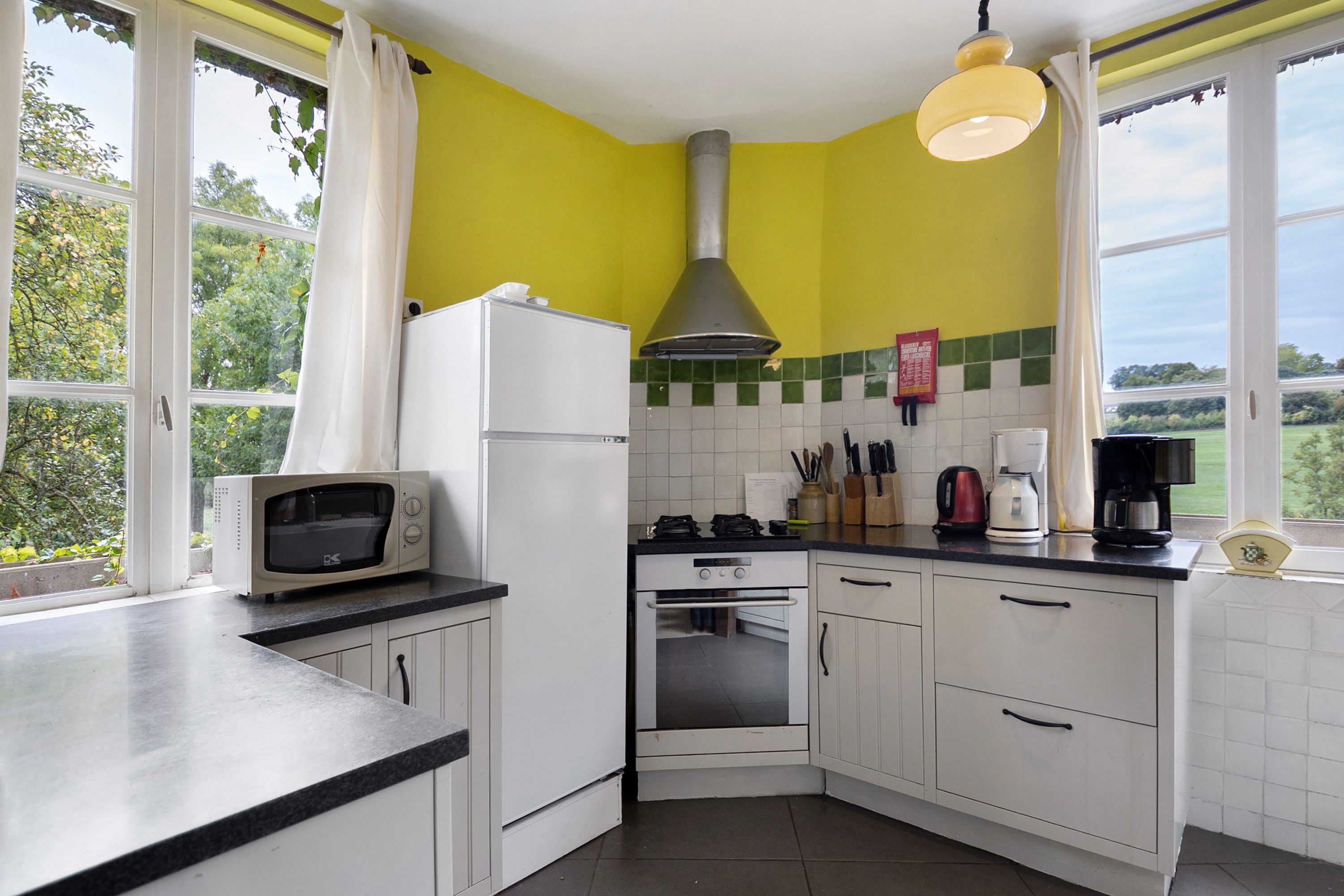 Een keuken met witte kastjes, een magnetron, een fornuis en een spoelbak.