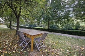 An outdoor wooden table with metal chairs, surrounded by grass and fallen leaves. - Cottage “La Cour Mare” with Private Pool, Terrace, and Wi-Fi (Crouttes)