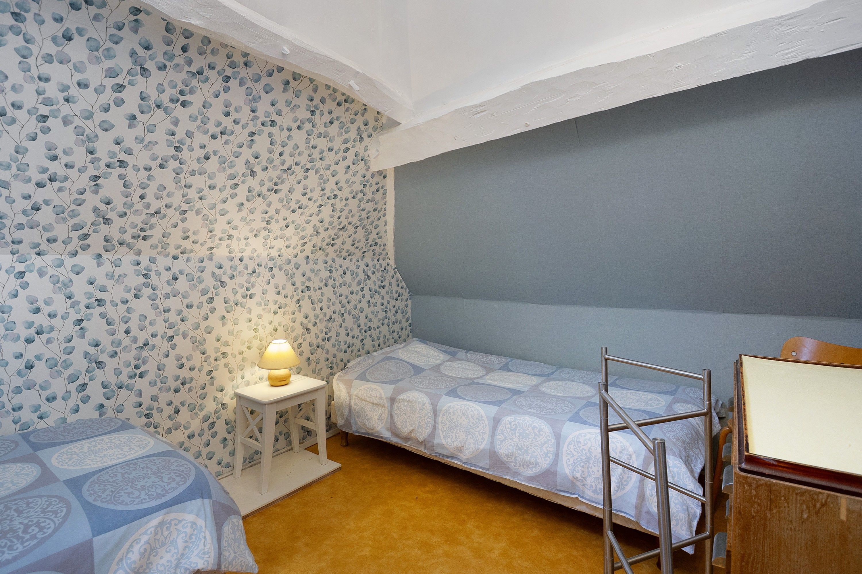 Een slaapkamer met twee eenpersoonsbedden, een nachtkastje met een lamp, en een ladder tegen de muur.