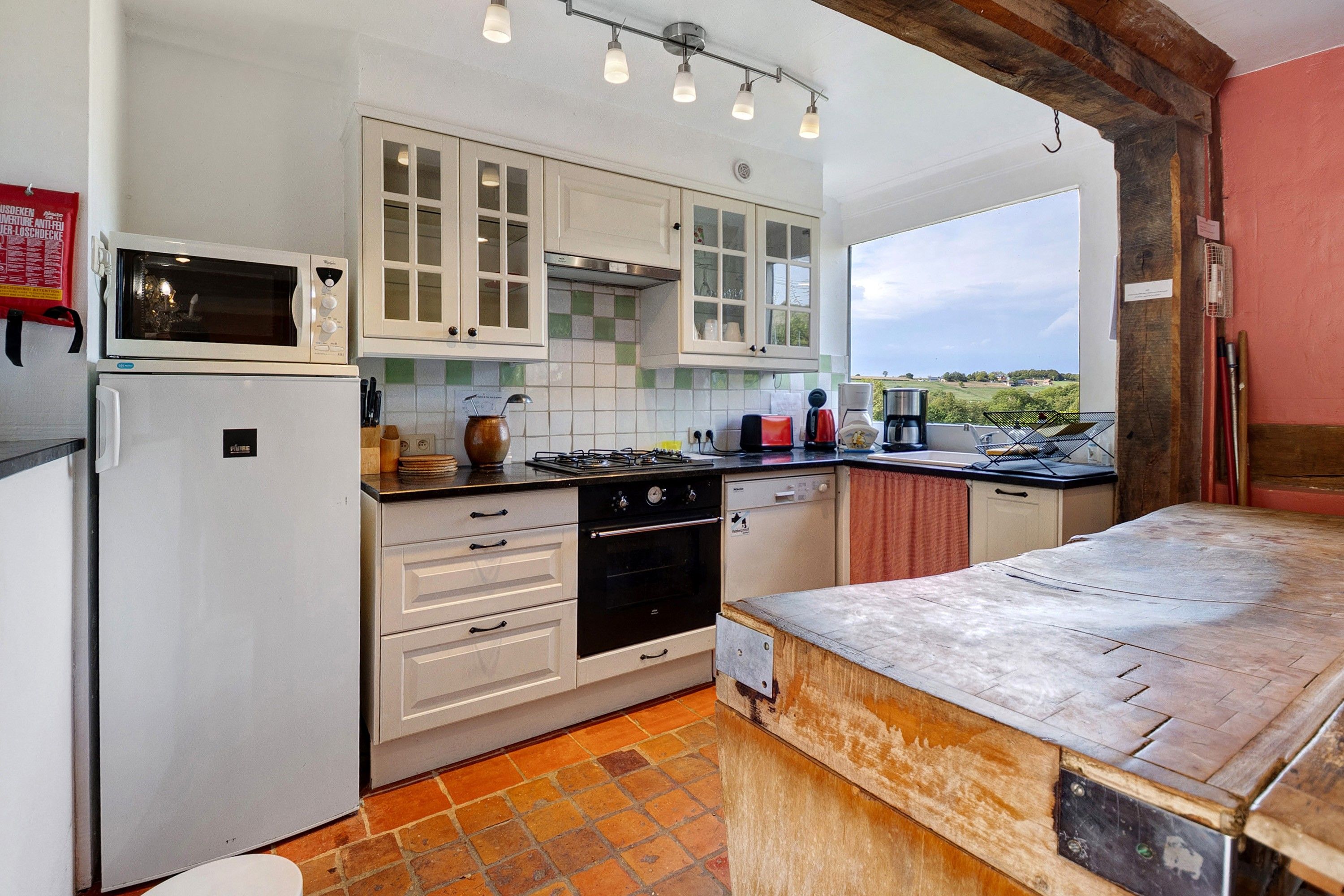 A kitchen with white cabinets, a microwave, a stove, and a view of the countryside.