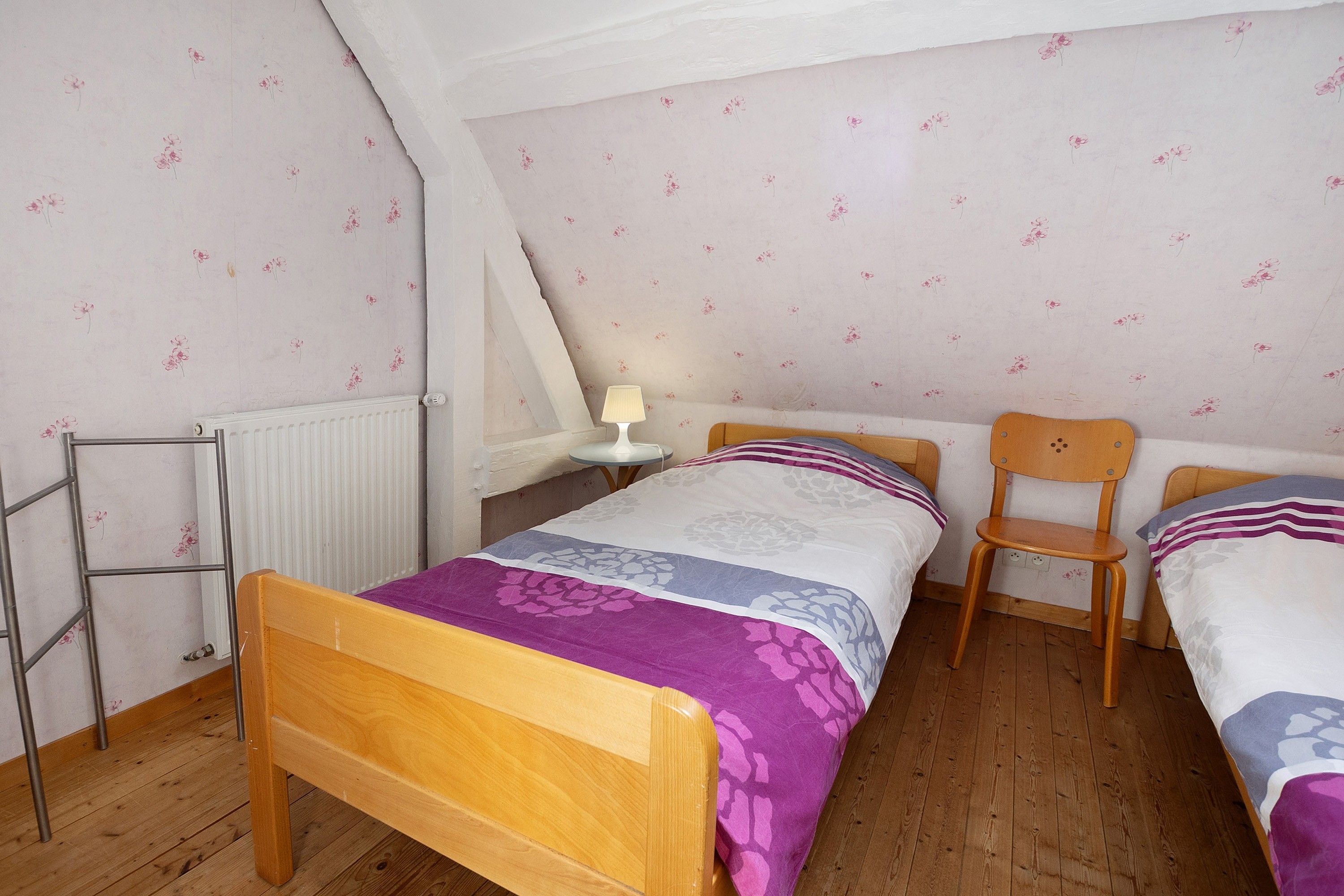 Ein Schlafzimmer mit einem hölzernen Bett, einem Sessel, einem kleinen Tisch mit einer Lampe und einer Heizung.