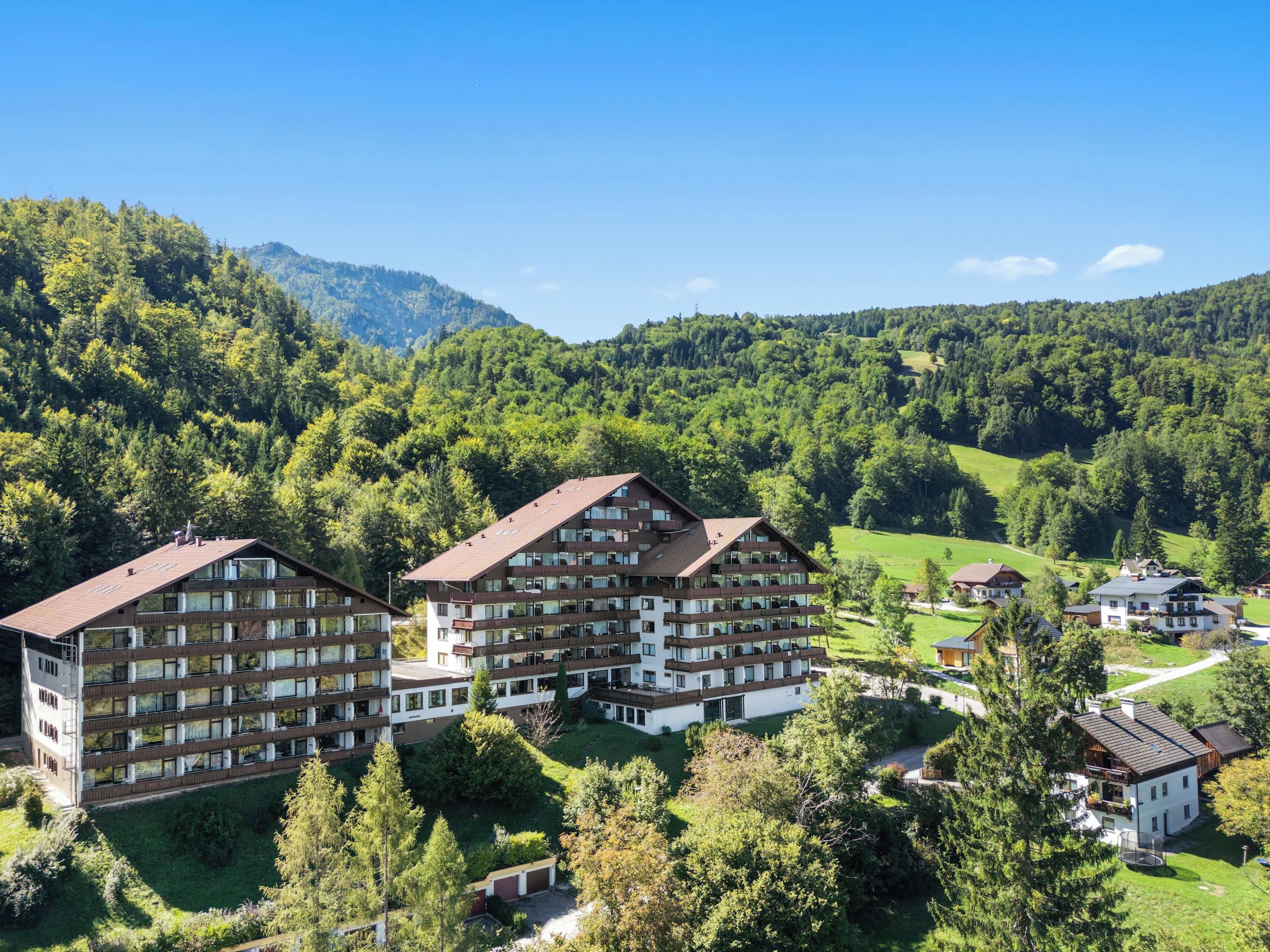 Ein mehrstöckiges Hotel mit Balkonen, umgeben von üppiger Vegetation und Bergen.