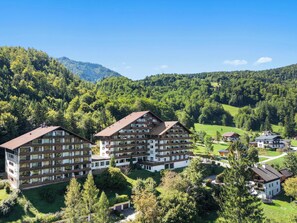A multi-story hotel with balconies, surrounded by lush greenery and mountains.