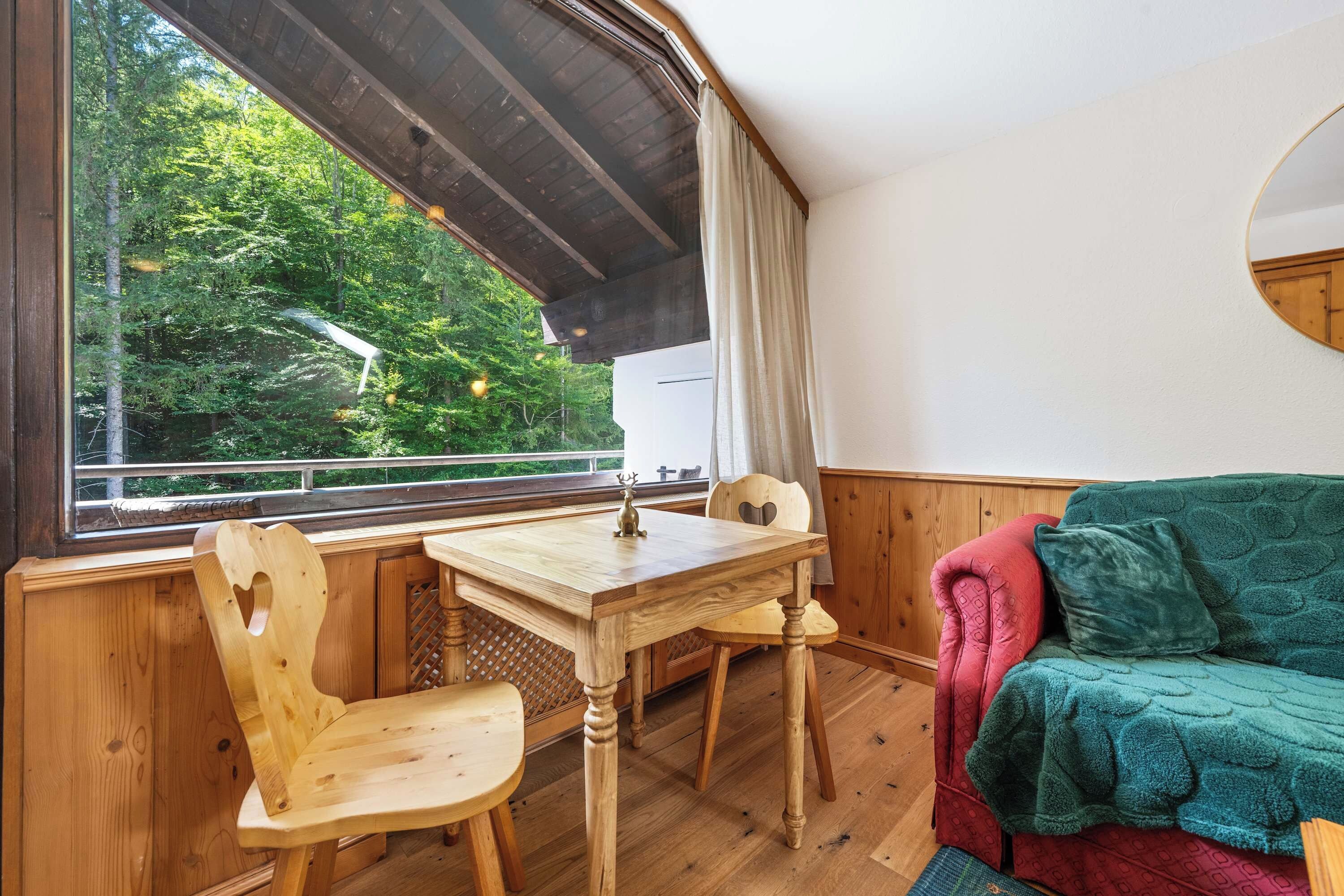 A cozy room with a wooden table and chairs, a window with a view of trees, and a green couch.