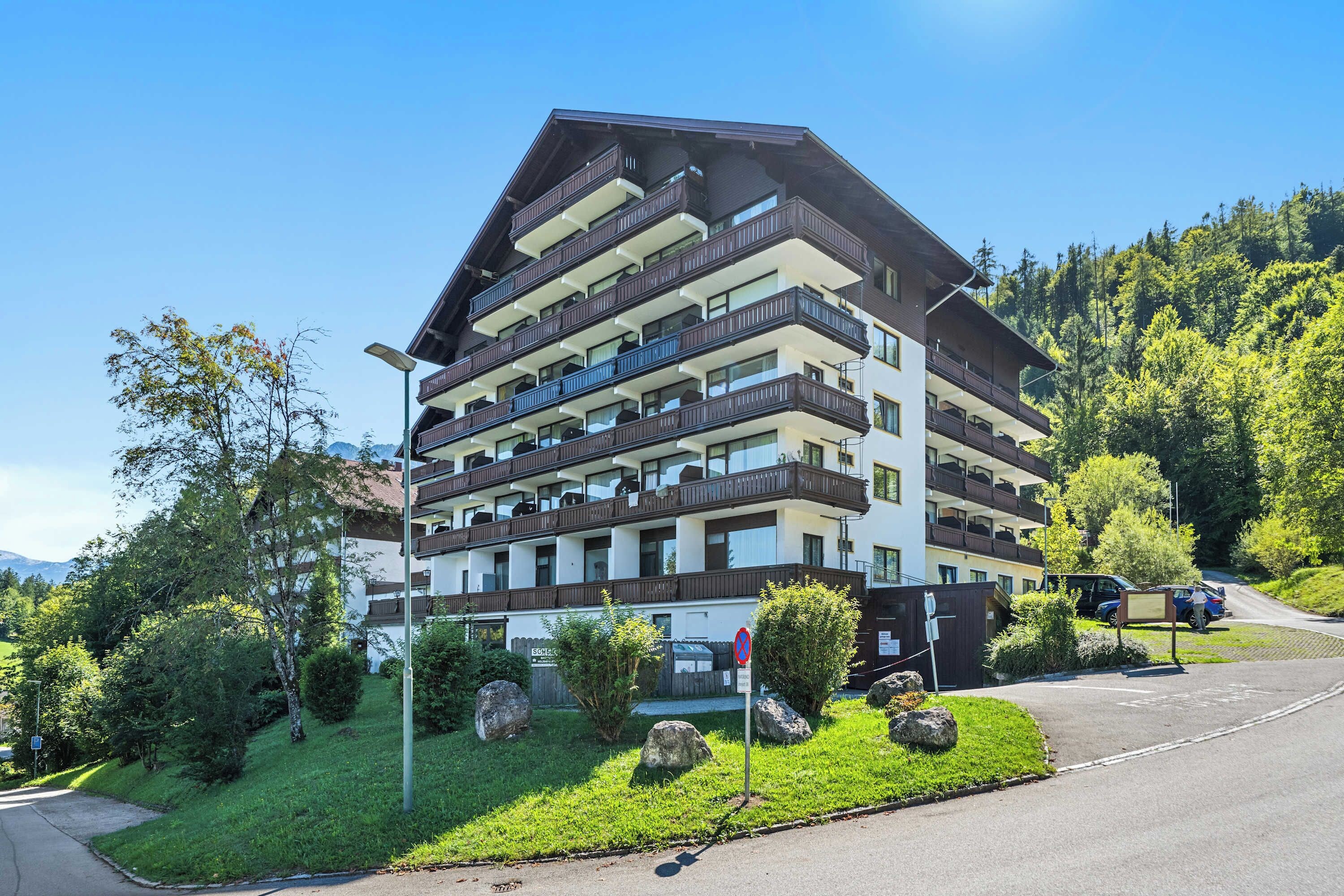 A multi-story hotel with balconies, surrounded by greenery and a mountainous backdrop.