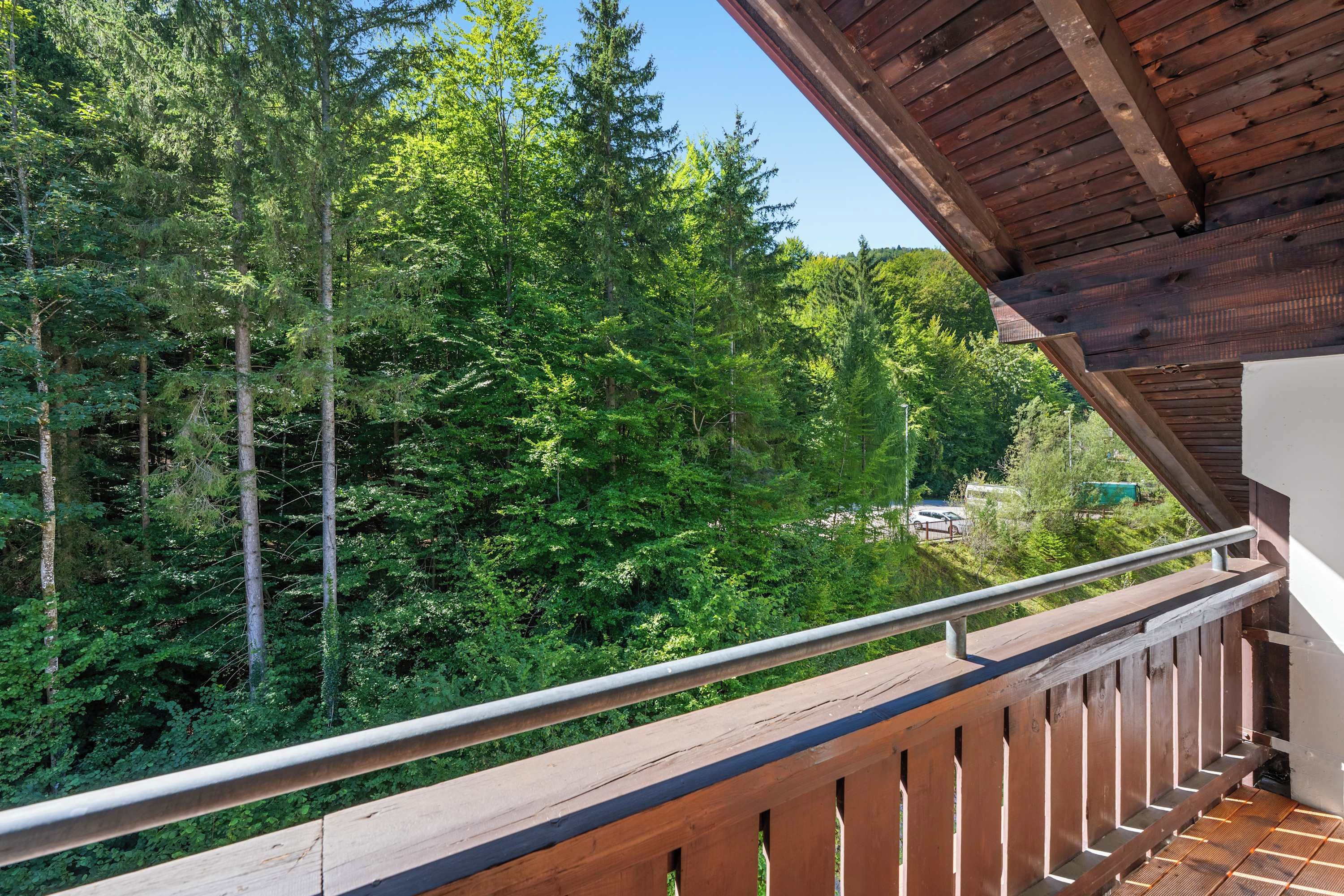 Ein Balkon mit Holzgeländer, der auf einen bewaldeten Bereich blickt.
