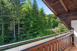 A balcony with a wooden railing overlooking a forested area.