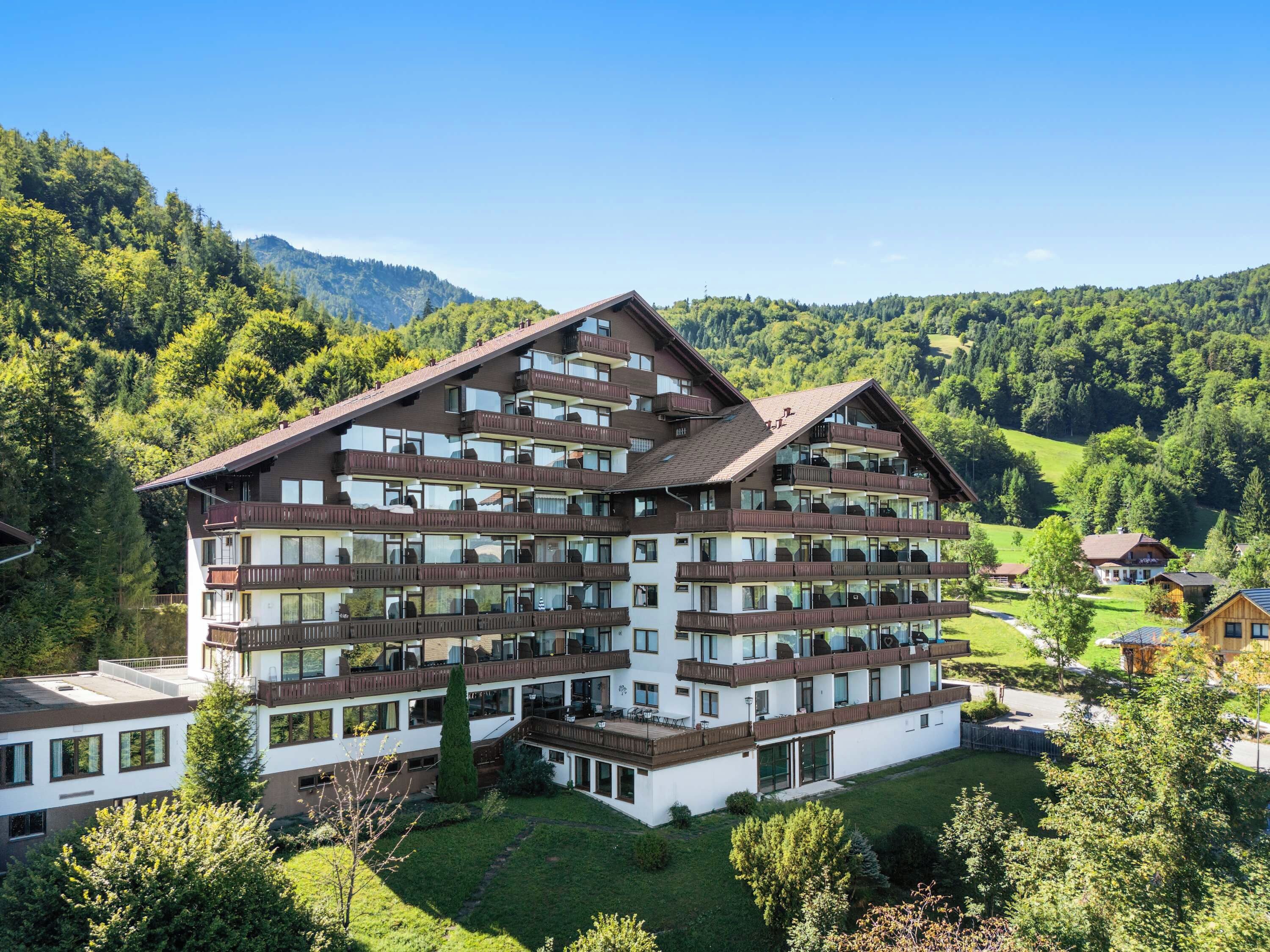 A multi-story hotel with balconies, surrounded by lush greenery and mountains.