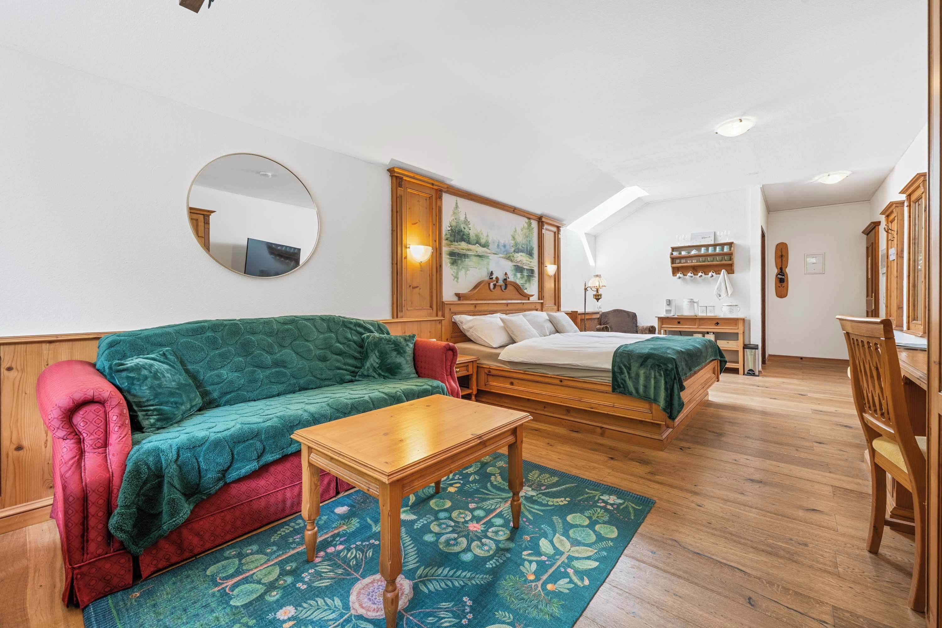 A cozy room with a bed, a sofa, a small table, and a mirror.
