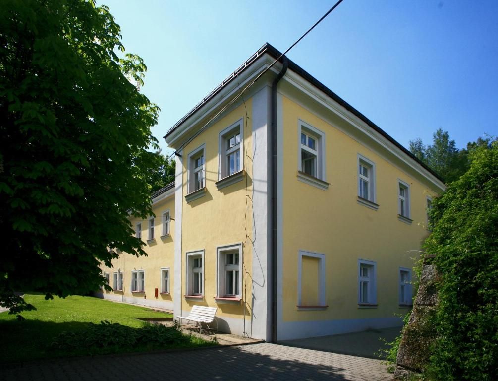 Un bâtiment jaune, doté de nombreuses fenêtres et d’une porte, entouré de verdure.