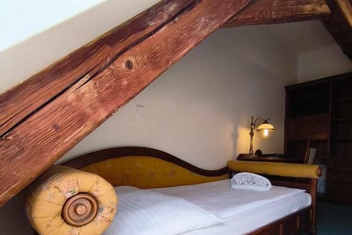 A wooden bed with a slanted ceiling, a bedside lamp, and a carpeted floor.