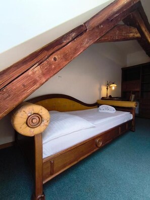 A wooden bed with a slanted ceiling, a bedside lamp, and a carpeted floor. - Depandance Vodoléčba (Lázně Libverda)