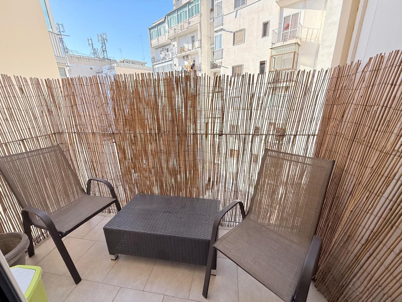 Eine Terrasse im Freien mit einem Bambuszaun, zwei Korbstühlen und einem kleinen Tisch.