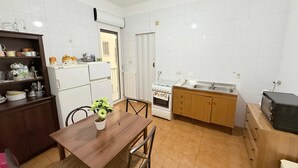 Een kleine keuken met witte betegelde wanden, een houten eettafel en een inbouwoven.