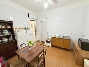 Cozinha compacta com paredes revestidas de azulejos brancos, uma mesa de jantar de madeira e um forno embutido.