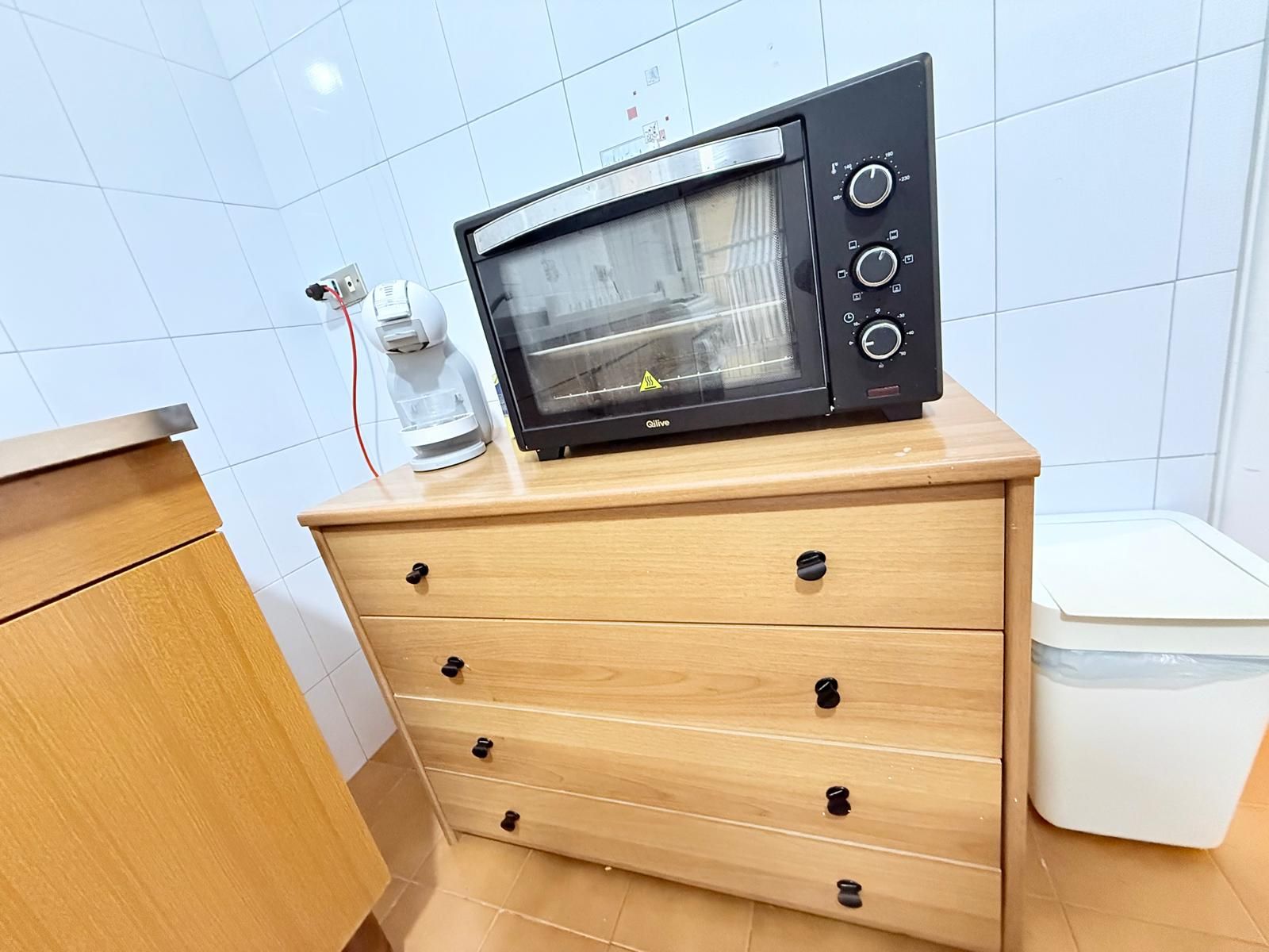 A kitchenette with a microwave oven on a wooden cabinet, a coffee maker, and a trash bin.