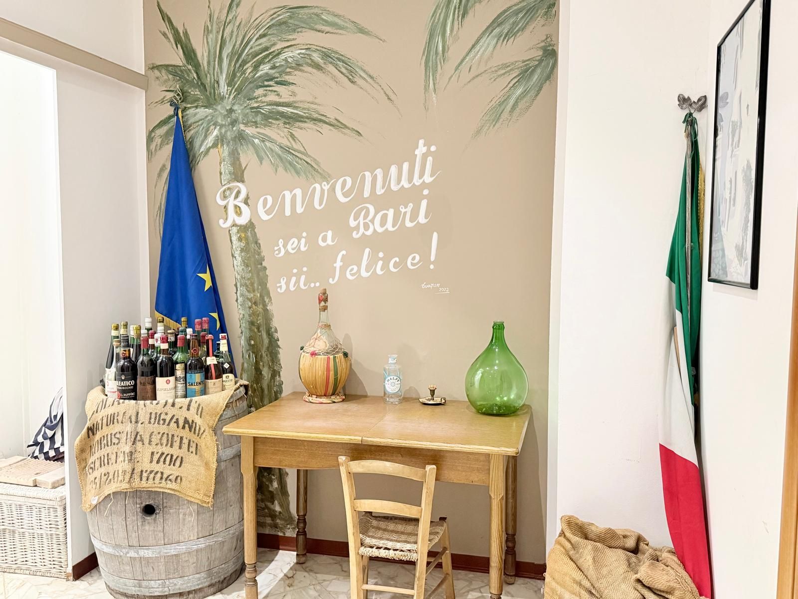 Una habitación con una mesa de madera, una silla, una botella de vino y una pared con un mural de palmeras y una bandera.