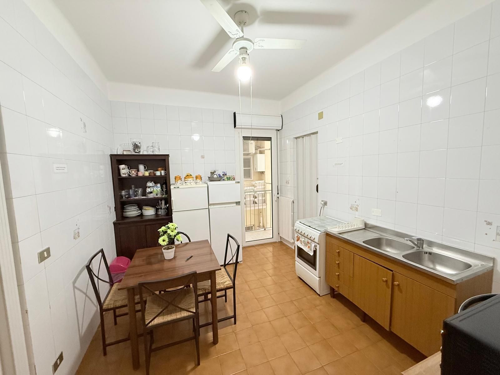 Una cocina compacta con baldosas blancas, una mesa de comedor con sillas, horno empotrado y refrigerador.