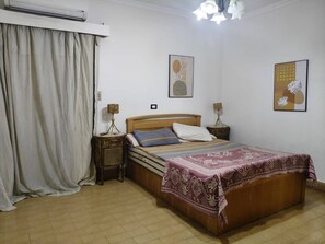 A bedroom with a wooden bed, two bedside tables, a floor lamp, and a bedspread. - Degla Maadi Urban Nest 3 Brm Apartment (Cairo)