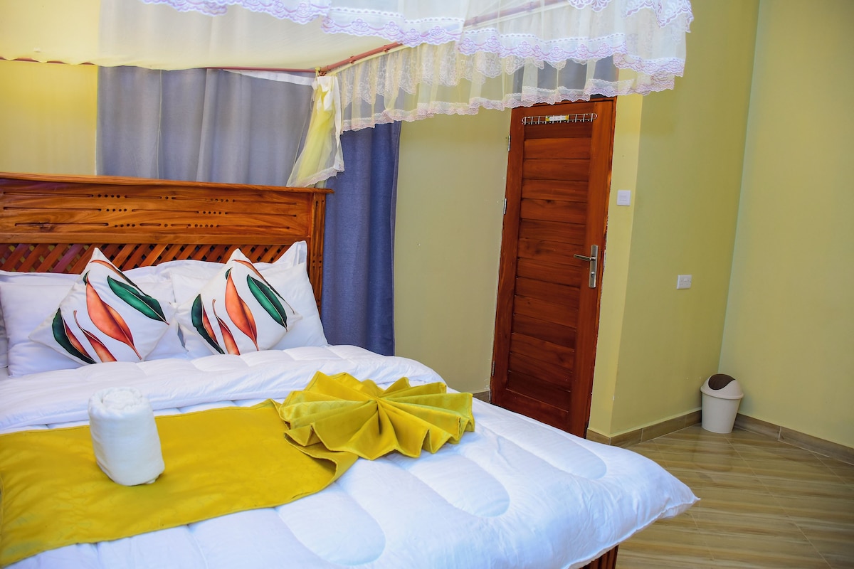 A neatly made bed with a yellow decorative pillow, a wooden headboard, and a lace canopy.