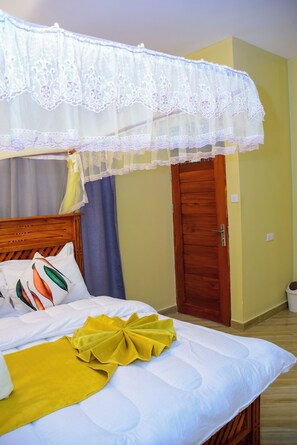A hotel room with a bed, a wooden door, and a window with curtains. - SOLOMON VILLAGE LODGE DODOMA (Dodoma)