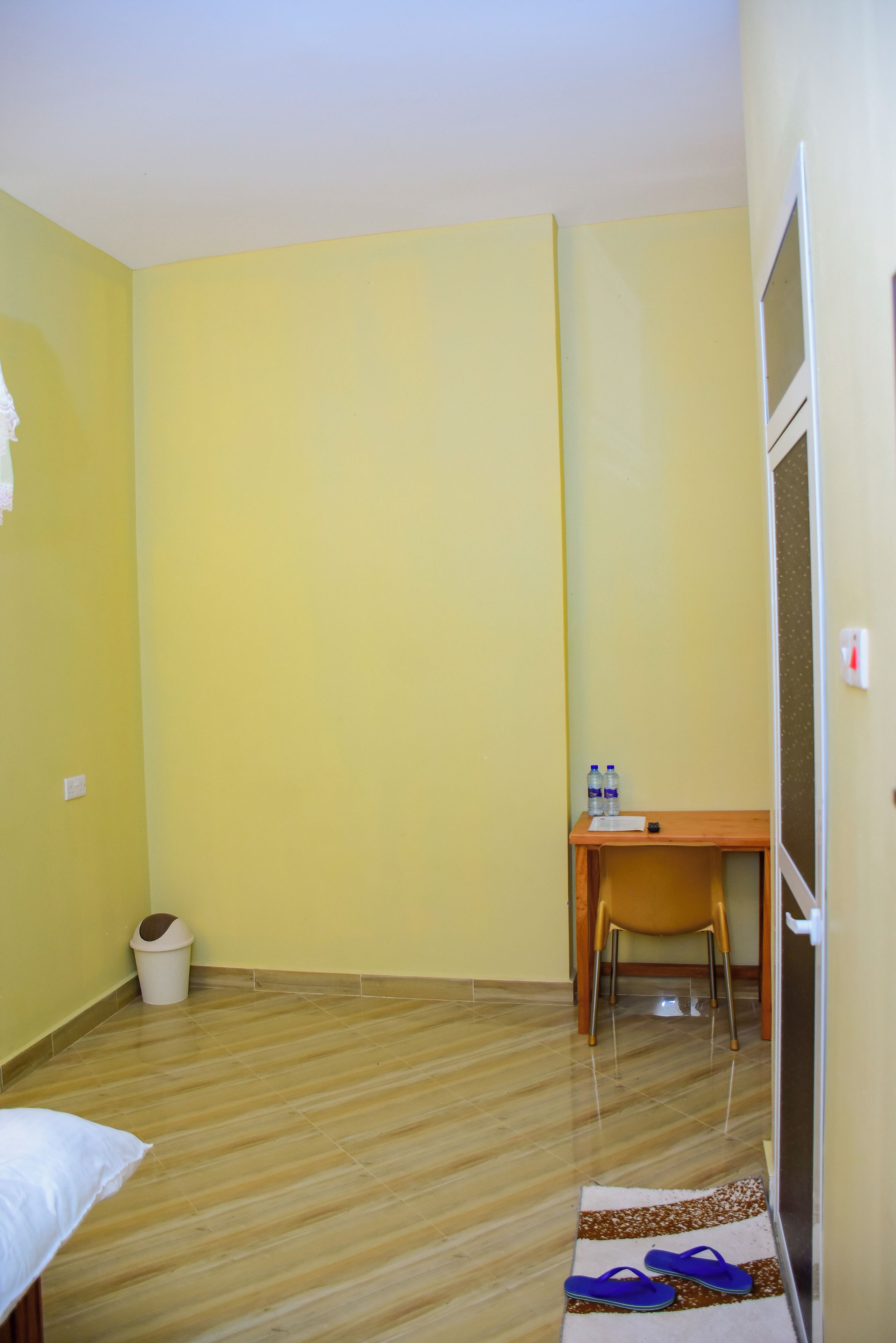 A room with a bed, a desk, a chair, a trash bin, and a water bottle.