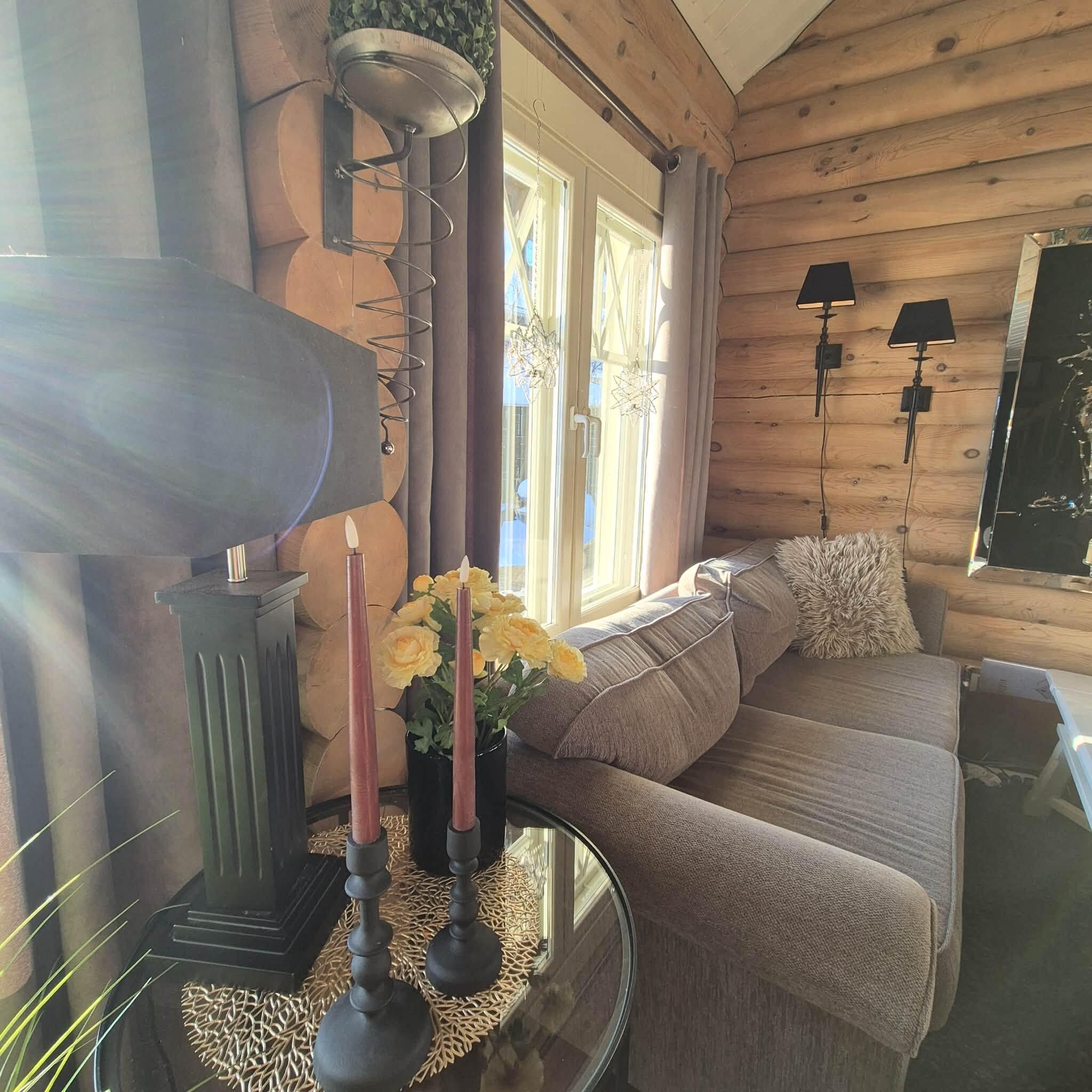 L’intérieur d’un chalet chaleureux, avec un canapé, une table décorée de bougies et une fenêtre ornée de rideaux.