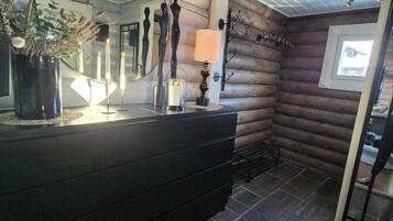 Interior de una cabaña de troncos con un tocador de madera oscura, un espejo y una ventana con vista a una casa.
