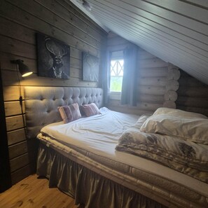A bedroom with a large bed, a headboard, and a window with curtains.