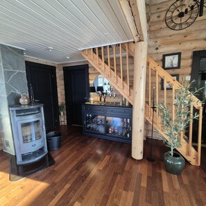 A wooden interior with a central staircase, a built-in wood stove, and a cabinet with glass doors.