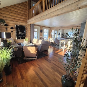 A spacious log cabin interior with a dining area, seating, and a kitchen.