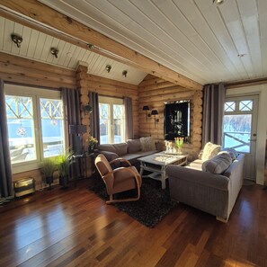A log cabin interior with a wooden floor, two sofas, a coffee table, and a fireplace.