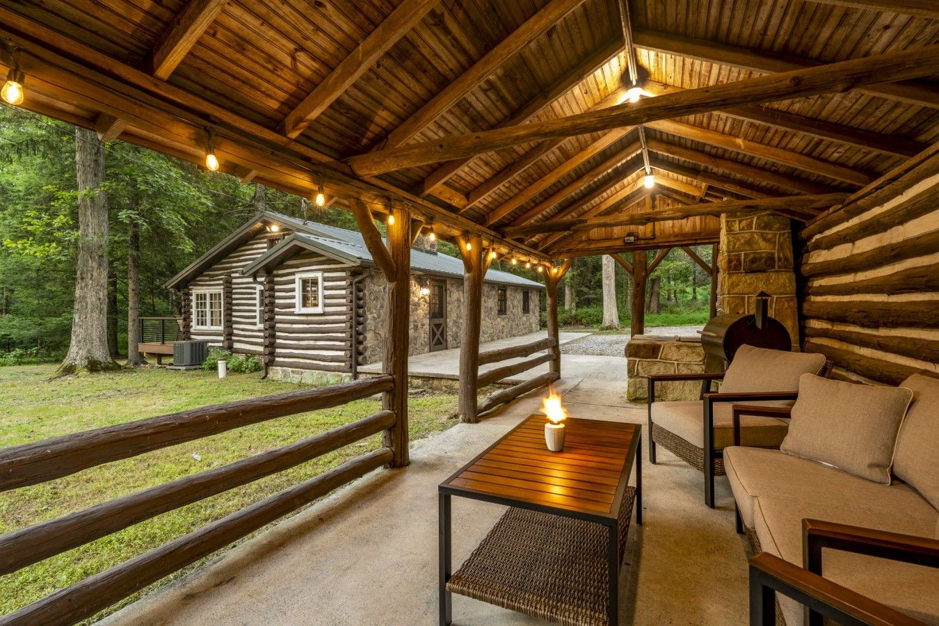 Un chalet rustique doté d’une terrasse en bois, d’une cheminée en pierre et d’un coin salon confortable avec une table et des chaises.