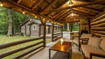 Un chalet rustique doté d’une terrasse en bois, d’une cheminée en pierre et d’un coin salon confortable avec une table et des chaises.