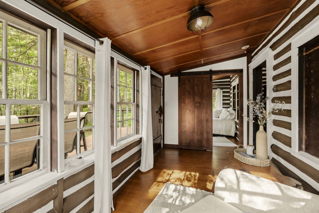 Un intérieur en bois avec un couloir menant à une chambre, de grandes fenêtres et un luminaire au plafond.