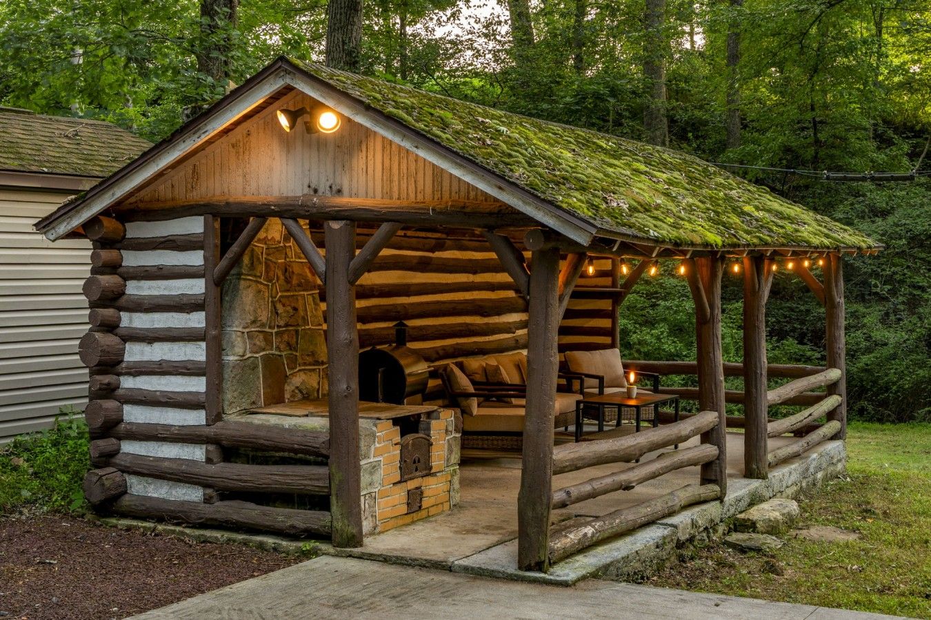 Une structure rustique en bois, dotée d’un mur en pierre, d’un four en briques et d’un espace détente avec des coussins.