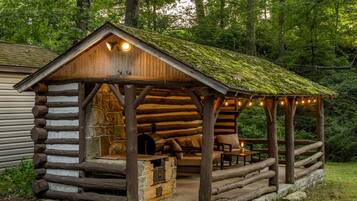 Une structure rustique en bois, dotée d’un mur en pierre, d’un four en briques et d’un espace détente avec des coussins.