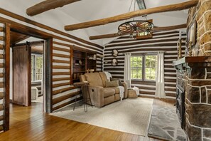 A log cabin interior with a fireplace, a sofa, and a wooden ceiling.