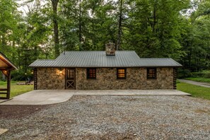 A stone building with a metal roof, a chimney, and a gravel driveway.