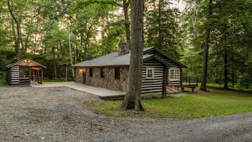 A rustic cabin with a stone exterior, a porch, and a bench in a forested area.