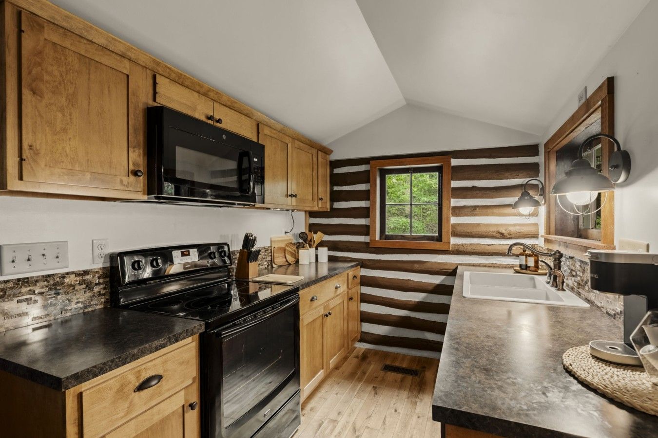 A kitchen with wooden cabinets, a black stove, a microwave, and a window with a view of greenery.