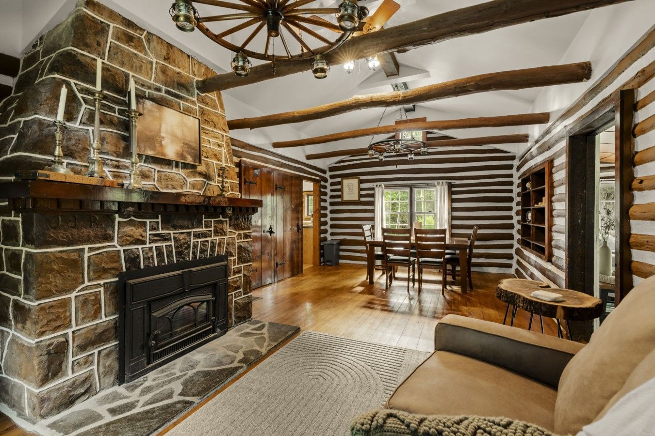 L’intérieur d’une cabane en rondins, avec une cheminée en pierre, des poutres en bois, un coin repas et un espace salon confortable.