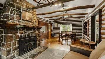 L’intérieur d’une cabane en rondins, avec une cheminée en pierre, des poutres en bois, un coin repas et un espace salon confortable.