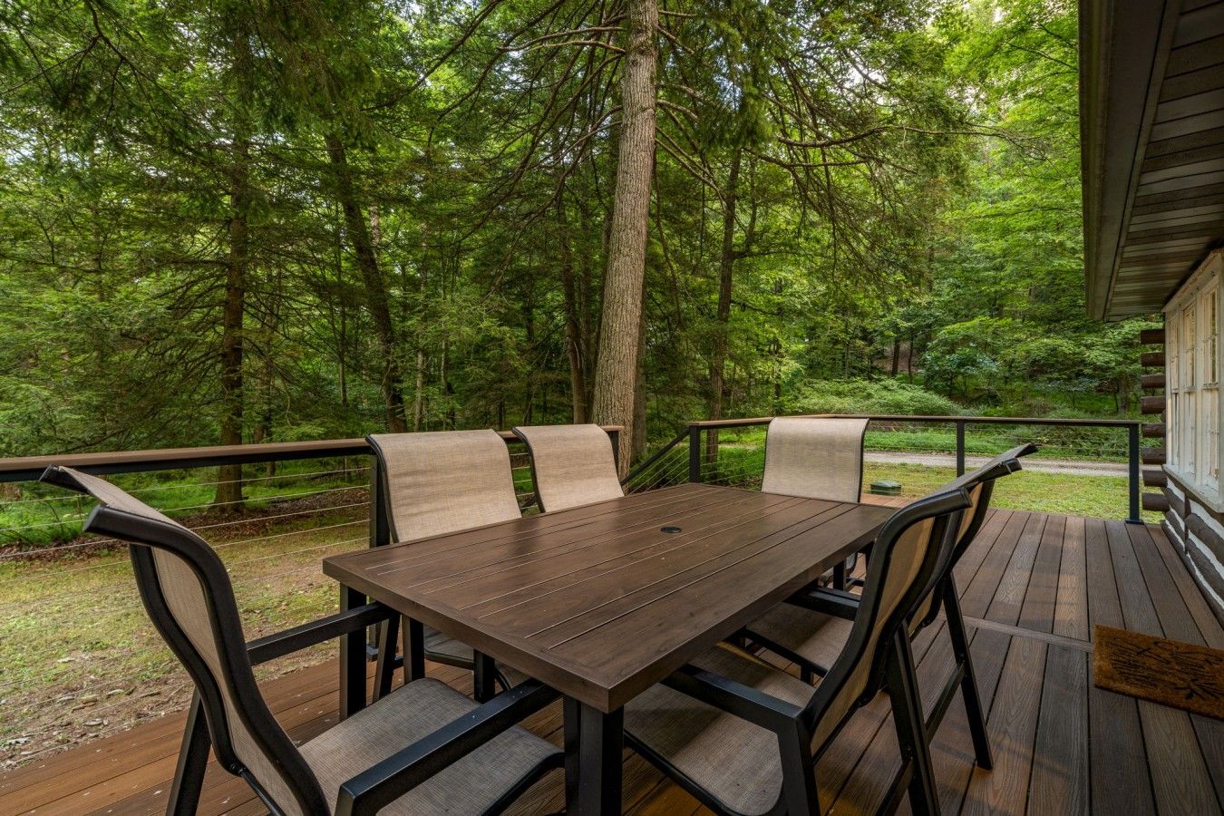 An outdoor wooden deck with a table and chairs, surrounded by a forest.