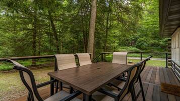 An outdoor wooden deck with a table and chairs, surrounded by a forest.