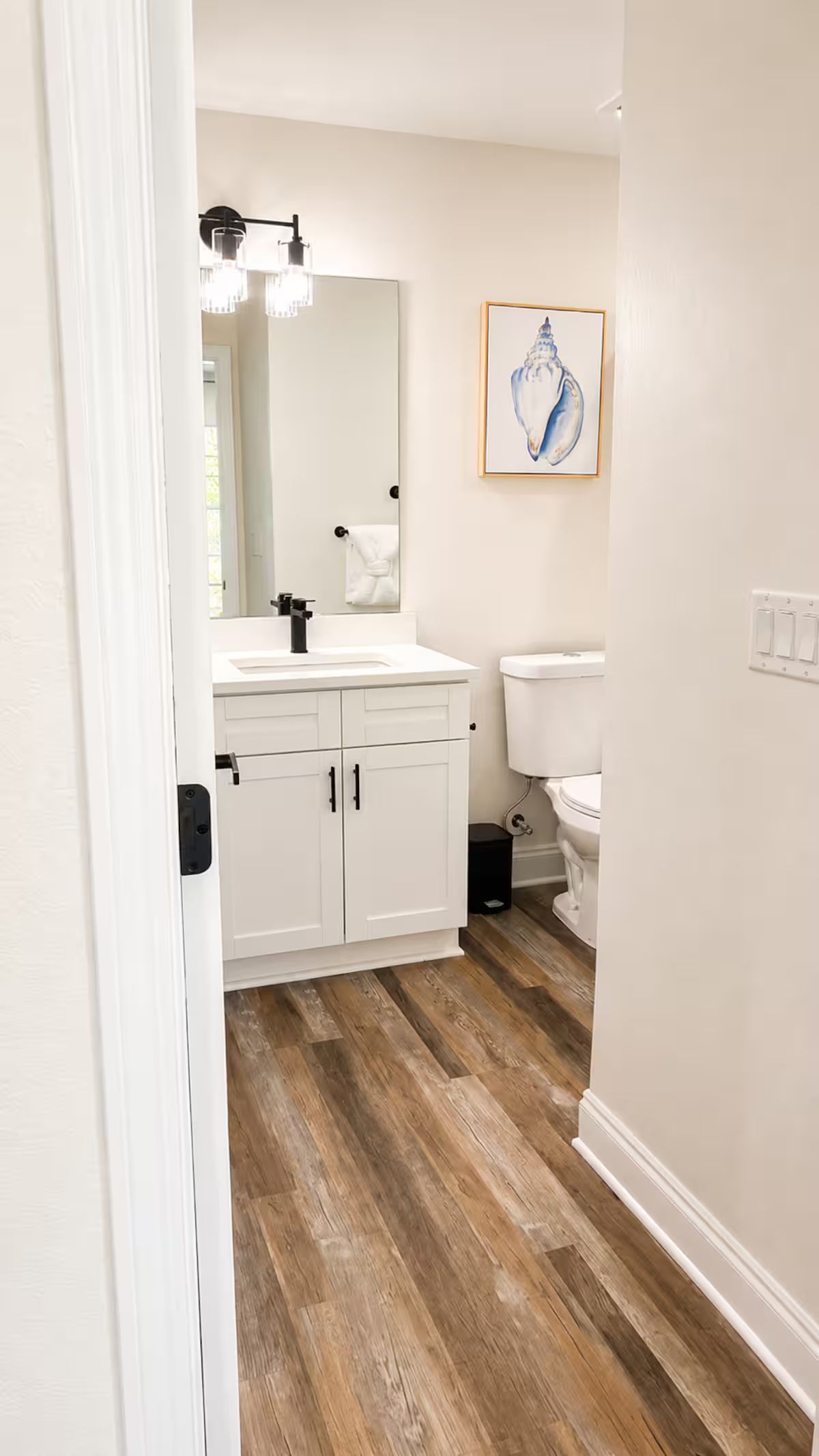 Une salle de bain avec un meuble-lavabo blanc, un miroir, des toilettes et une œuvre d’art encadrée accrochée au mur.