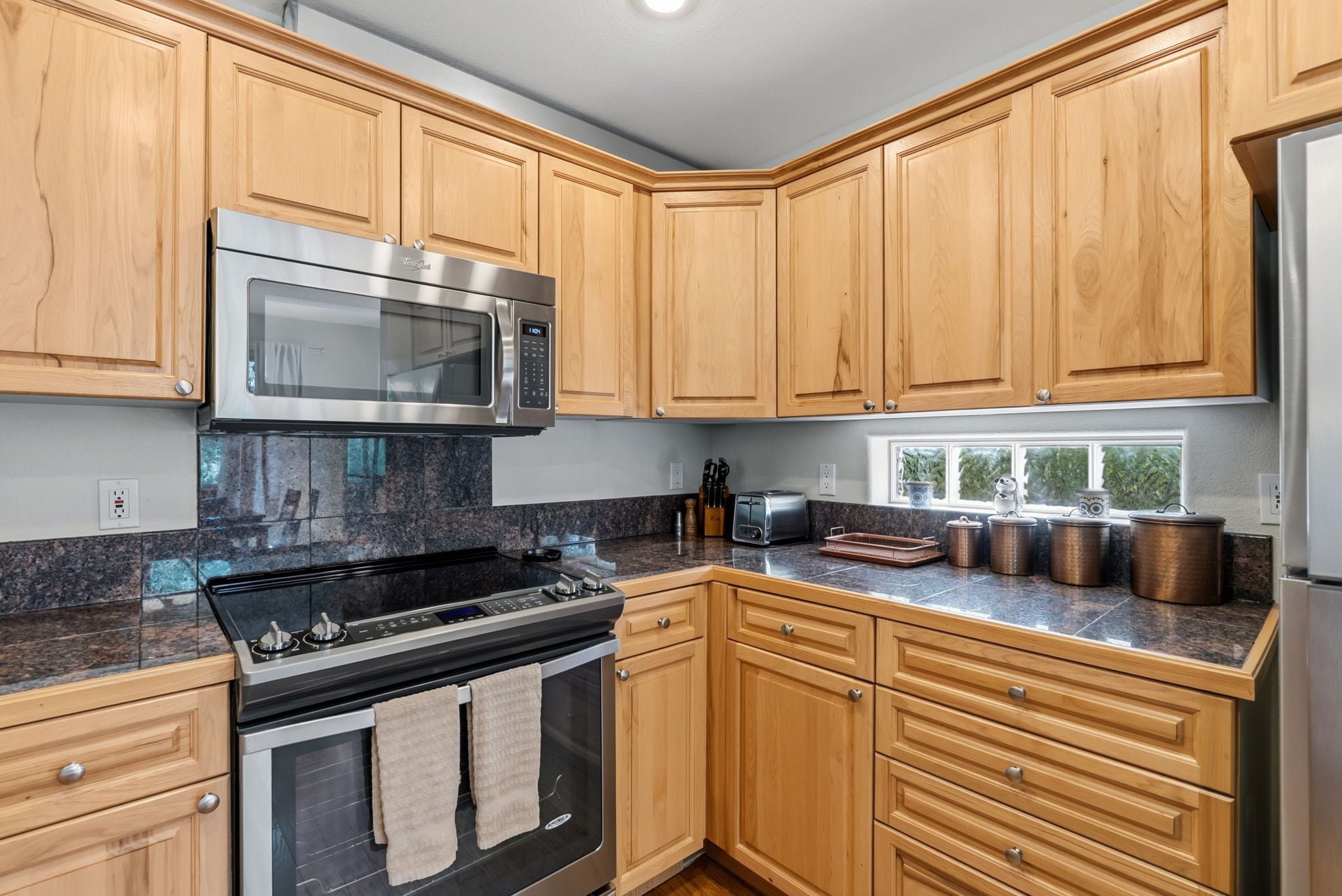 A kitchen with wooden cabinets, a stainless steel microwave, a gas stove, and a refrigerator.